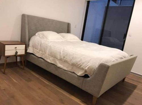 ein Bett mit grauem Rahmen und einem Nachttisch neben einem Fenster in der Unterkunft Estudio vacacional in Puerto Peñasco