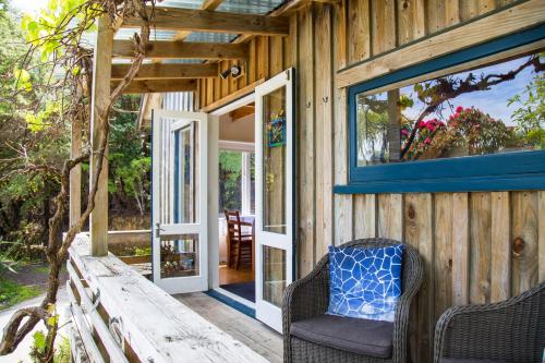 a wooden house with a door and two chairs on a porch at Fern Lodge Coromandel in Coromandel Town