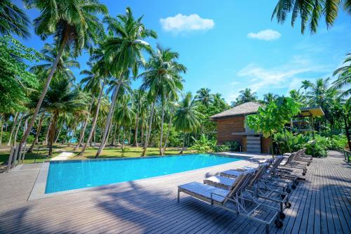 a resort pool with lounge chairs and palm trees at Tilar Siro Andamans - CGH Earth in Havelock Island