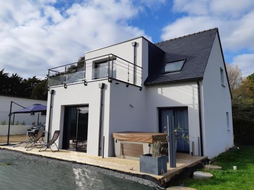 ein weißes Haus mit einer Holzterrasse neben einem Wasserkörper in der Unterkunft Maison à 200m des plages avec jacuzzi in Trégunc