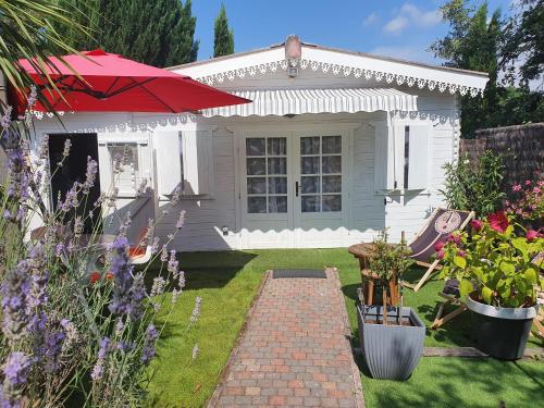 a small white house with a red umbrella in the yard at Chalet Cosy in Audenge