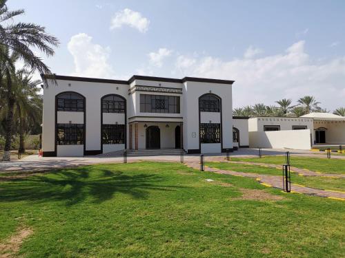 a large white building with large windows and a yard at بيت العز السياحي Al-Ezz Tourist House in Sohar