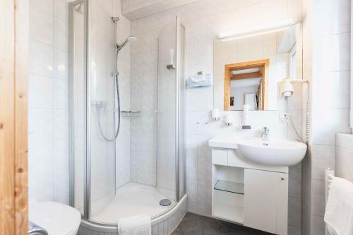 a white bathroom with a shower and a sink at Hotel Bellevue in Bad Wiessee