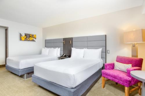 a hotel room with two beds and a pink chair at Crowne Plaza San Jose La Sabana by IHG in San José