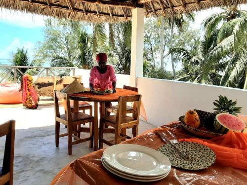 a woman sitting at a table with plates on it at Ayla Beach House in Kiwengwa