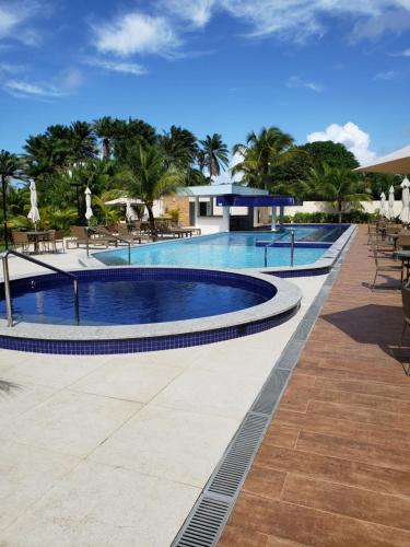 a pool at a resort with tables and chairs at Flat em Guarajuba, Paraíso dos Coqueiros in Guarajuba