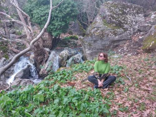 a woman sitting on the ground next to a waterfall at Drosostalida in Áno Sími