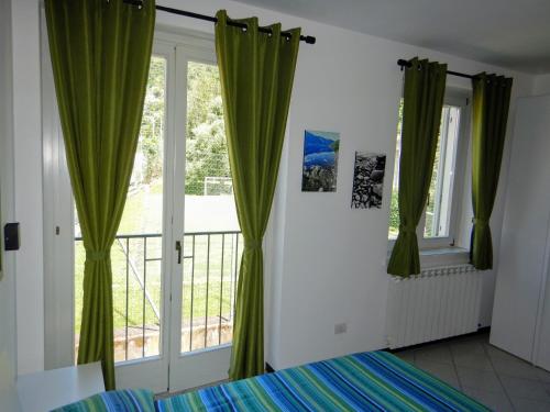 - une chambre avec des rideaux verts, un lit et un balcon dans l'établissement Green Relax in Maccagno, à Maccagno Inferiore