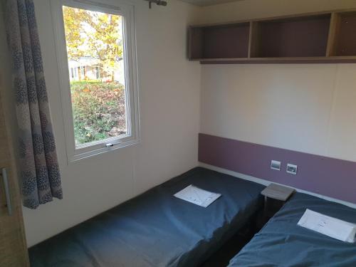 Cette petite chambre comprend un lit bleu et une fenêtre. dans l'établissement Camping Marvilla Parks - Rivages des Landes - Mobil home 3 chambres, à Aureilhan