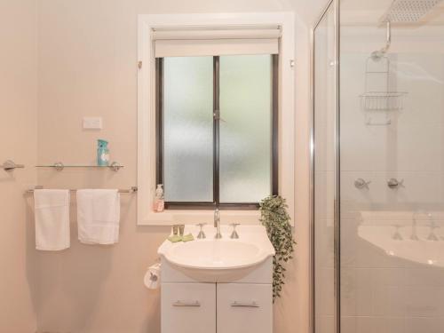La salle de bains blanche est pourvue d'un lavabo et d'une douche. dans l'établissement Jackson Hole 3, à Jindabyne