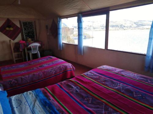 two beds in a room with a view of the water at Uros Suyawi Titicaca Lodge in Puno
