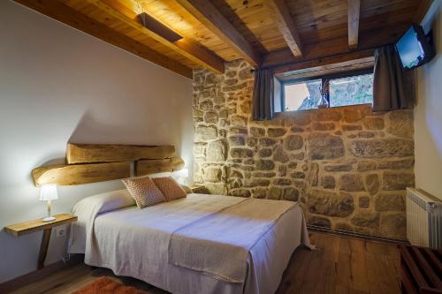 1 dormitorio con cama y pared de piedra en El Sitio de Carmelo, en Cuzcurrita de Río Tirón