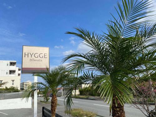 two palm trees in front of a sign on a street at HYGGE Biimata in Nago