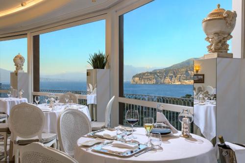 a restaurant with white tables and chairs and a view of the ocean at Grand Hotel Capodimonte in Sorrento