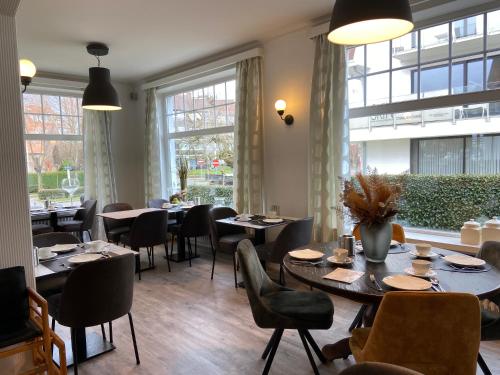a dining room with tables and chairs and windows at Hotel Les Arcades in Knokke-Heist