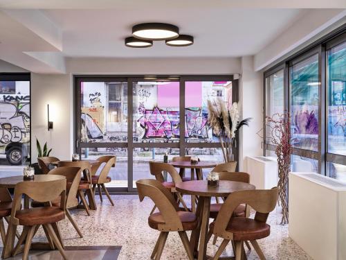 um restaurante com mesas, cadeiras e janelas em NLH KERAMEIKOS - Neighborhood Lifestyle Hotels em Atenas
