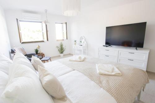 a white bedroom with a large white bed and a flat screen tv at Kuća u centru in Pakoštane