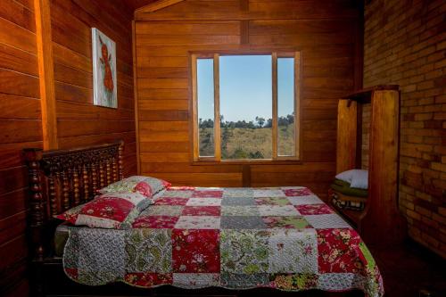 a bedroom with a quilt on a bed with a window at Chalés Belo Vale - Ibitipoca in Conceição da Ibitipoca