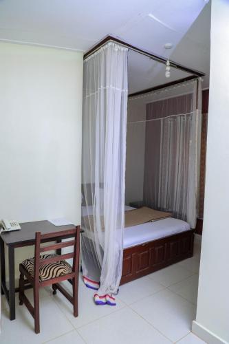 a bed in a room with a table and a chair at Royal Park Hotel in Jinja