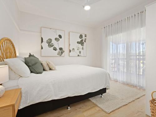 a white bedroom with a bed and a window at Husky Beach House by Experience Jervis Bay in Huskisson