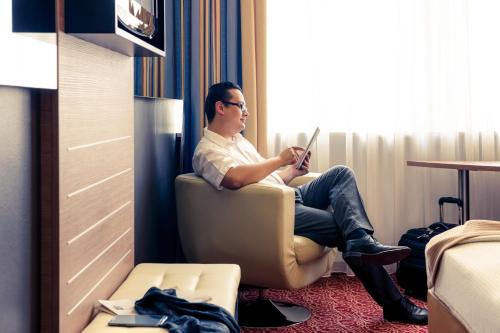 a man sitting in a chair in a room with a tablet at Mercure Hotel Kaiserhof City Center in Frankfurt/Main