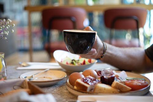 a person holding a cup of coffee over a table with food at Old Port Hotel in Limassol
