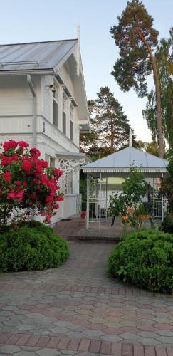 a white house with red flowers in front of it at Naiza Guesthouse and Apartments in Jūrmala