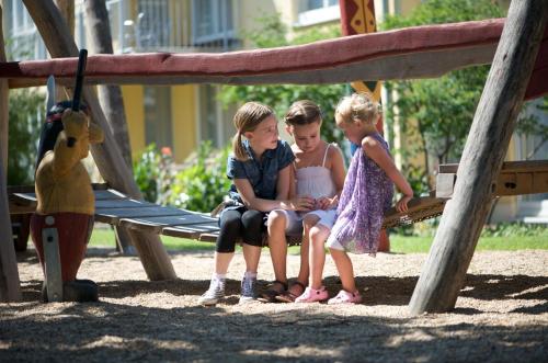 two girls sitting on a bench in a playground at City Hotel Dresden Radebeul in Radebeul