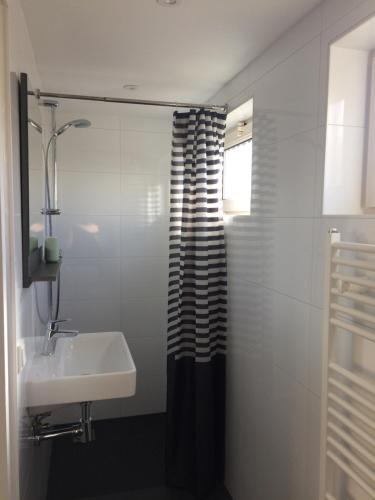 baño con cortina de ducha en blanco y negro y lavamanos en Zomerhuis Zuid 1, en Egmond aan Zee