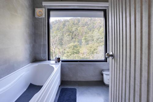 a bathroom with a large tub and a window at SaffronStays Elysian, Dehradun - best mountain views from this party - All clear roads in Dehradun