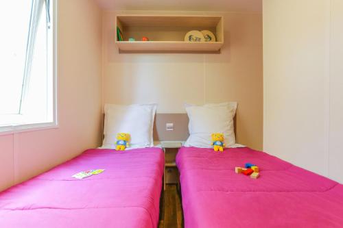 Duas camas num pequeno quarto com lençóis cor-de-rosa em Camping maeva Escapades Le Colomba em Olmeto