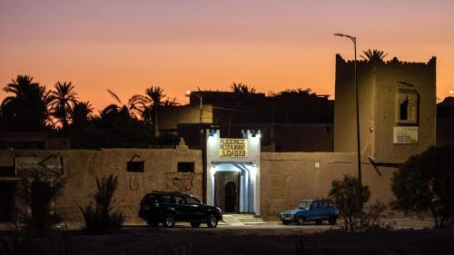 two cars parked in front of a building with a sign at Auberge L'Oasis in Foum Zguid