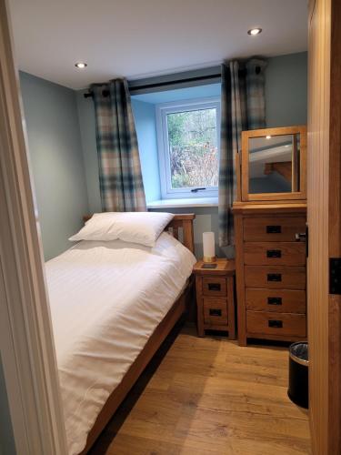 a bedroom with a bed and a dresser and a window at The Granary in Llanddeiniol