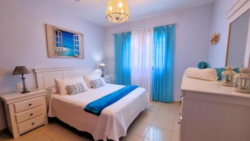 a bedroom with a white bed and blue curtains at La Graciosa Mykonos Beach, Junior Suite in Caleta de Sebo