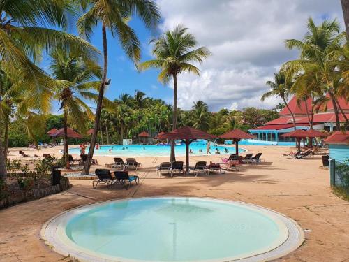 una grande piscina accanto a una spiaggia con palme di Martial Tropiques et Martial Coco & Plage, 2 Appartements refaits à neuf vue mer, Village de vacances à Ste Anne a Sainte-Anne