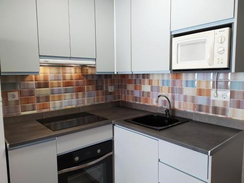 a kitchen with white cabinets and a sink and a microwave at Urbanización la barca in Oropesa del Mar