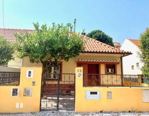 ein gelbes Haus mit einem Baum und einem Zaun in der Unterkunft TOP BEACH HOUSE in Costa da Caparica