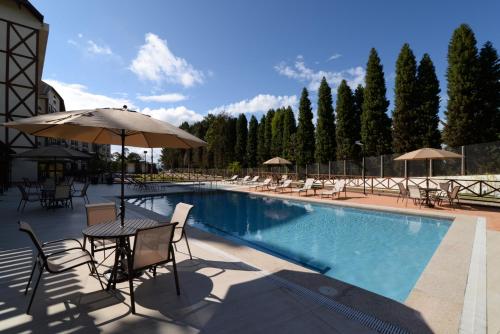 een zwembad met stoelen en tafels en een parasol bij Vista Azul Apart Hotel - Vista Pinheiros in Aracê