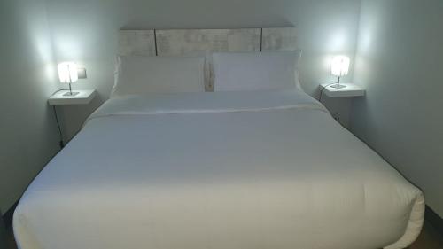 a large white bed with two lamps on the sides at H La Cabaña in Pozuelo de Alarcón