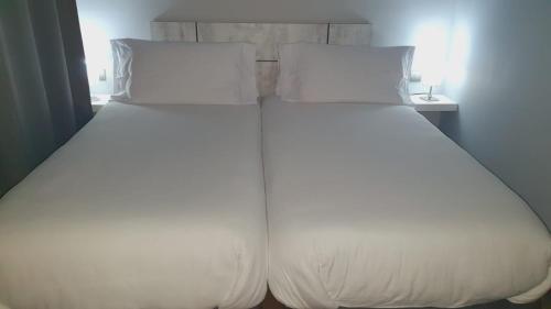 a large bed with white sheets and pillows at H La Cabaña in Pozuelo de Alarcón