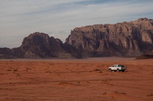 a white truck parked in the desert with mountains at Wadi Rum Nights in Wadi Rum