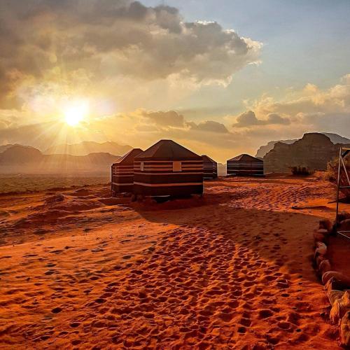 a desert with tents and the sun in the sky at Wadi Rum Nights in Wadi Rum