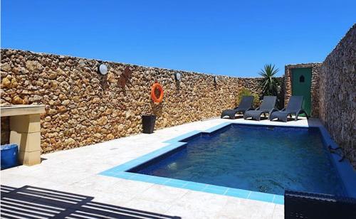 a swimming pool with chairs and a stone wall at Petra Farmhouse B&B in Nadur