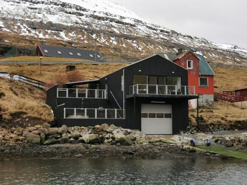 a black house with a red building on a hill at A pearl in a forgotten fjord - Luxury Boathouse in Funningsfjørður