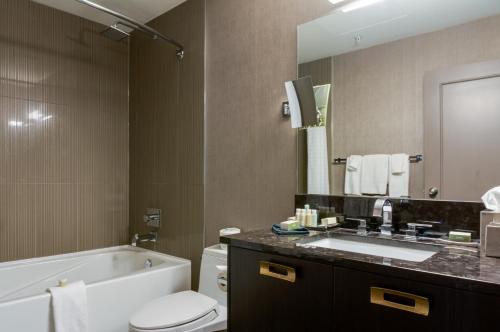 a bathroom with a tub and a toilet and a sink at Hotel Arts Kensington in Calgary