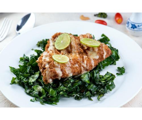 a white plate with a piece of fish and greens at Nirvana Beach Resort, Koh Lanta SHA Extra Plus in Ko Lanta