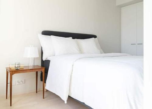 a bed with white sheets and a table with a lamp at Stylish new 1br apt in Aurinkolahti in Helsinki