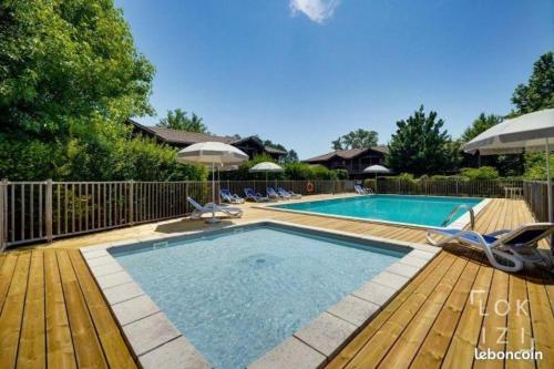 una piscina con sillas y sombrillas en una terraza de madera en Bel appartement cosy dans résidence avec piscine 5 minutes plage, en Messanges