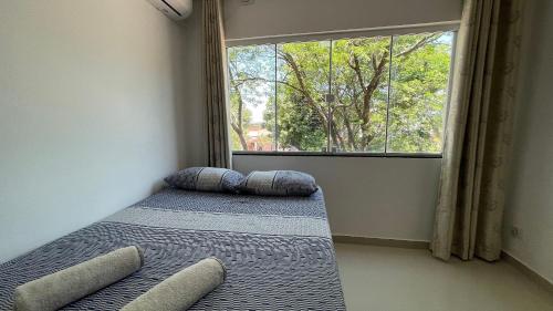 1 dormitorio con cama con almohadas y ventana en Sua casa em Foz do Iguaçu. Apt encantador e aconchegante na Vila A. en Foz de Iguazú