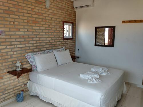 a bedroom with a white bed with a brick wall at Vila Beija-flor in Canoa Quebrada